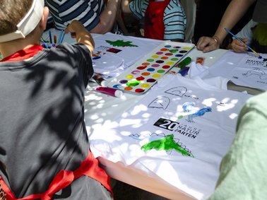 Mehrere Kinder sitzen an einem Tisch und bemalen ihre eigenen T-Shirts