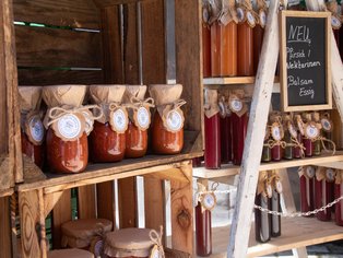 Regal mit Gläsern gefüllt mit roten und braunen Lebensmitteln, daneben ein kleines schwarzes Schild mit weißer Schrift