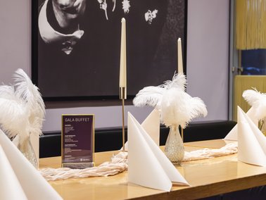 Weiße Schale mit gelbem Nudelsalat, garniert mit frischen Kräutern, auf dunklem Tuch neben Holzbrett mit Eierscheiben.