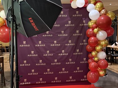Fotostudio mit rotem Teppich, schwarzem Hintergrund mit weißem Logo und rotem, weißem sowie goldenem Ballonbogen.