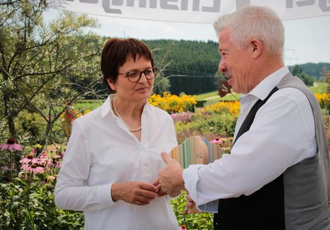 Zwei Personen im Gespräch bei der Auszeichnung eines Gartens im Rahmen der UN-Dekade Biologische Vielfalt, umgeben von blühenden Pflanzen und grüner Landschaft