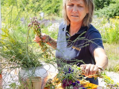 Person bindet draußen bunte Blumenkränze mit verschiedenen Wildblumen und Gräsern