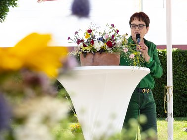 Frau Freidler hält Ihre Begrüßungsrede an einem Stehtisch im Freien.