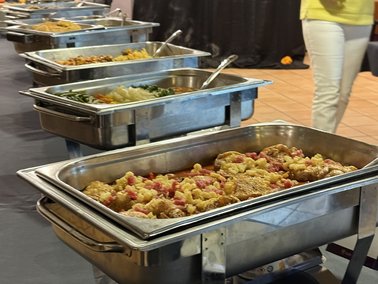 Mehrere Edelstahl-Warmhaltebehälter mit verschiedenen Speisen in Buffetreihe.