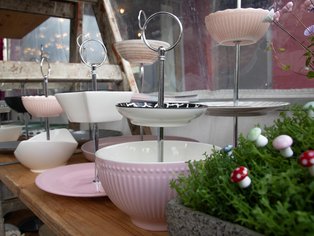 Mehrstöckige Etagere mit runden, geriffelten und glatten Schalen aus Keramik in Pastelltönen auf einem Holztisch neben einem Blumentopf mit Moos und Deko-Pilzen.