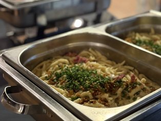 Metallbehälter mit Spaghetti, garniert mit gehackten Kräutern, in einem Buffet-Setup.