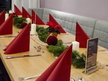 Langer Tisch mit rot gefalteten Servietten, weißen Kerzen und Tannengrün als Weihnachtsdekoration.