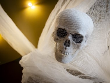 Weißer Totenschädel, der in weißem, durchscheinendem Stoff eingehüllt ist, mit gelbem Licht im Hintergrund.