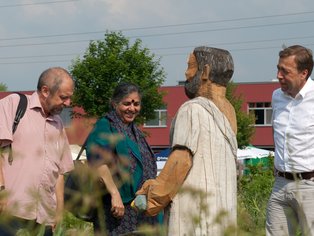 Drei fröhliche Menschen, die um eine Holzskulptur stehen.