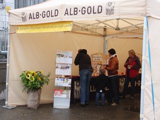 Marktstand von ALB-GOLD mit Kunden und Produkten.