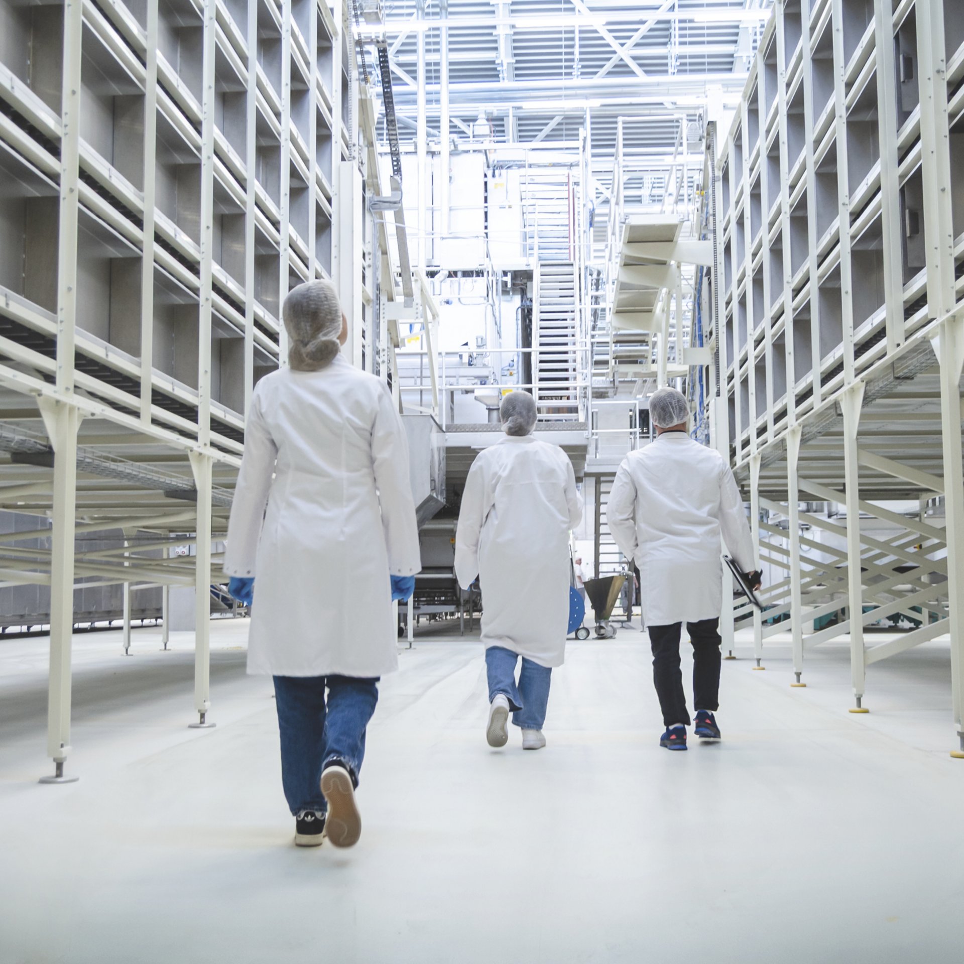 Drei Menschen in Schutzkleidung, die durch die Lagerhallen laufen. Drei Menschen in Schutzkleidung, die durch die Lagerhallen laufen.