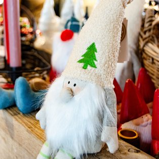 Weihnachtswichtel mit langem weißem Bart, spitzem weißem Hut mit grünem Tannenbaum und gestreiften Beinen sitzt auf einer Holzfläche