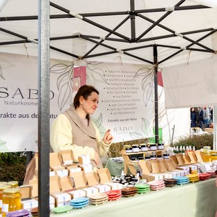 Zwei Frauen unter einem weißen Marktstand mit Naturkosmetikprodukten auf einem Tisch