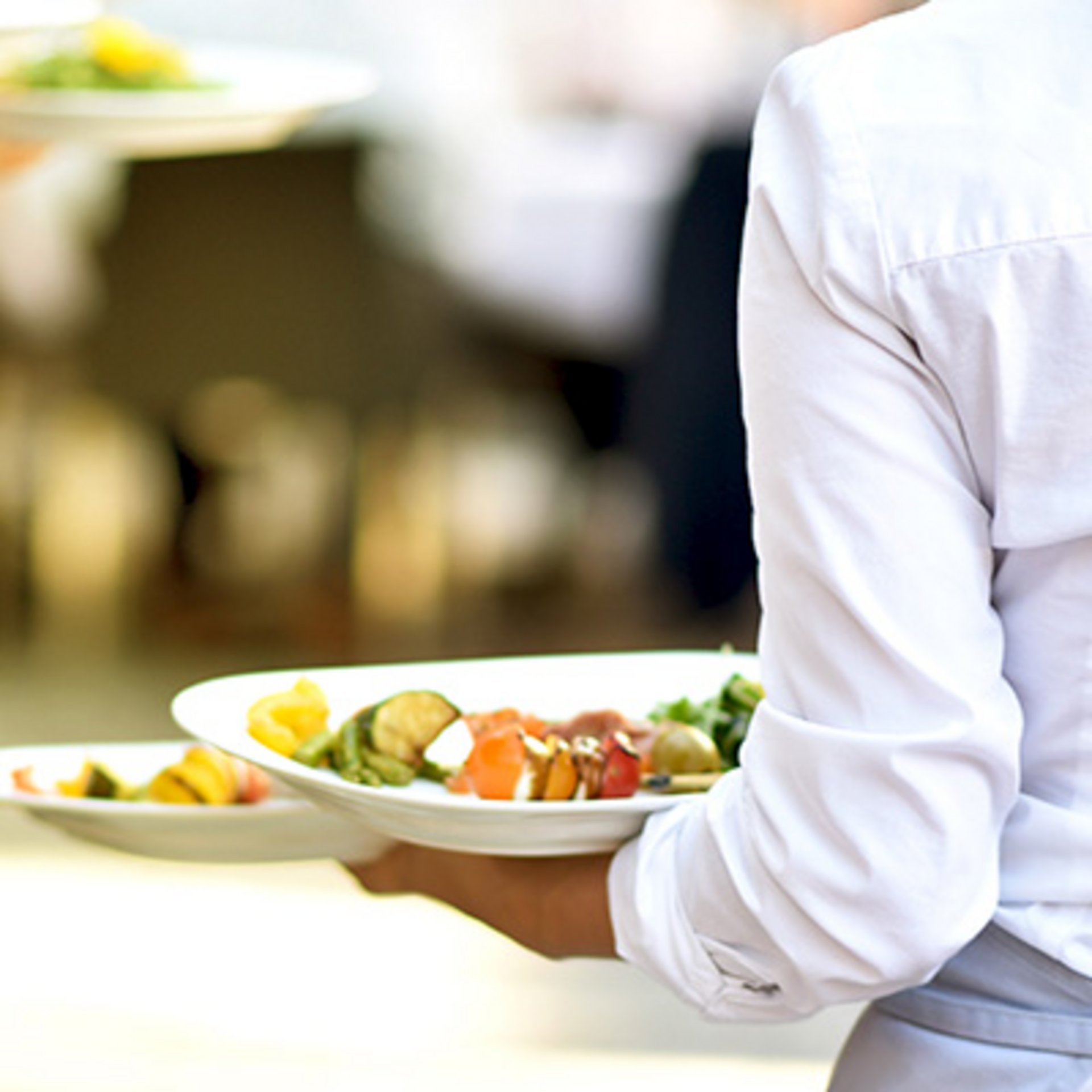 Eine Servicekraft, die zwei Teller auf ihrem linken Arm trägt. Eine Servicekraft, die zwei Teller auf ihrem linken Arm trägt.