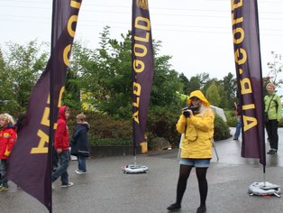 Fotograf in gelber Jacke beim Kinderfest mit Fahnen im Hintergrund.