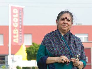 Vandana Shiva steht vor dem ALB-GOLD Gebäude, hinter ihr sieht man die ALB-GOLD Fahne.