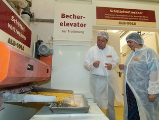 Personen stehen vor der Nudelmaschine, ein Mann erklärt etwas über die Produktion.