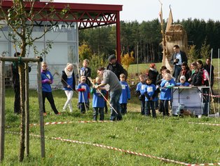 Kinder und Erwachsene bei einem Outdoor-Event auf einer Wiese mit einem großen Drachen und einem Zelt im Hintergrund
