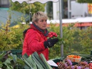 Eine Frau steht hinter einem Gemüse Verkaufsstand und präsentiert ihre Ware.