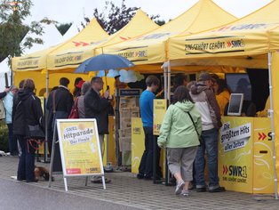 Menschen stehen an einem gelben Messestand von SWR 3 mit Informationsmaterial.