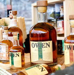 Mehrere Flaschen mit braunem Inhalt und Etiketten mit der Aufschrift 'OWEN' stehen auf einem Marktstand