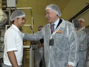 Der Bundespräsident bei einer Produktionsbesichtigung in Schutzkleidung, sein Arm liegt auf der Schulter eines Mitarbeiters und lacht dabei herzlich.