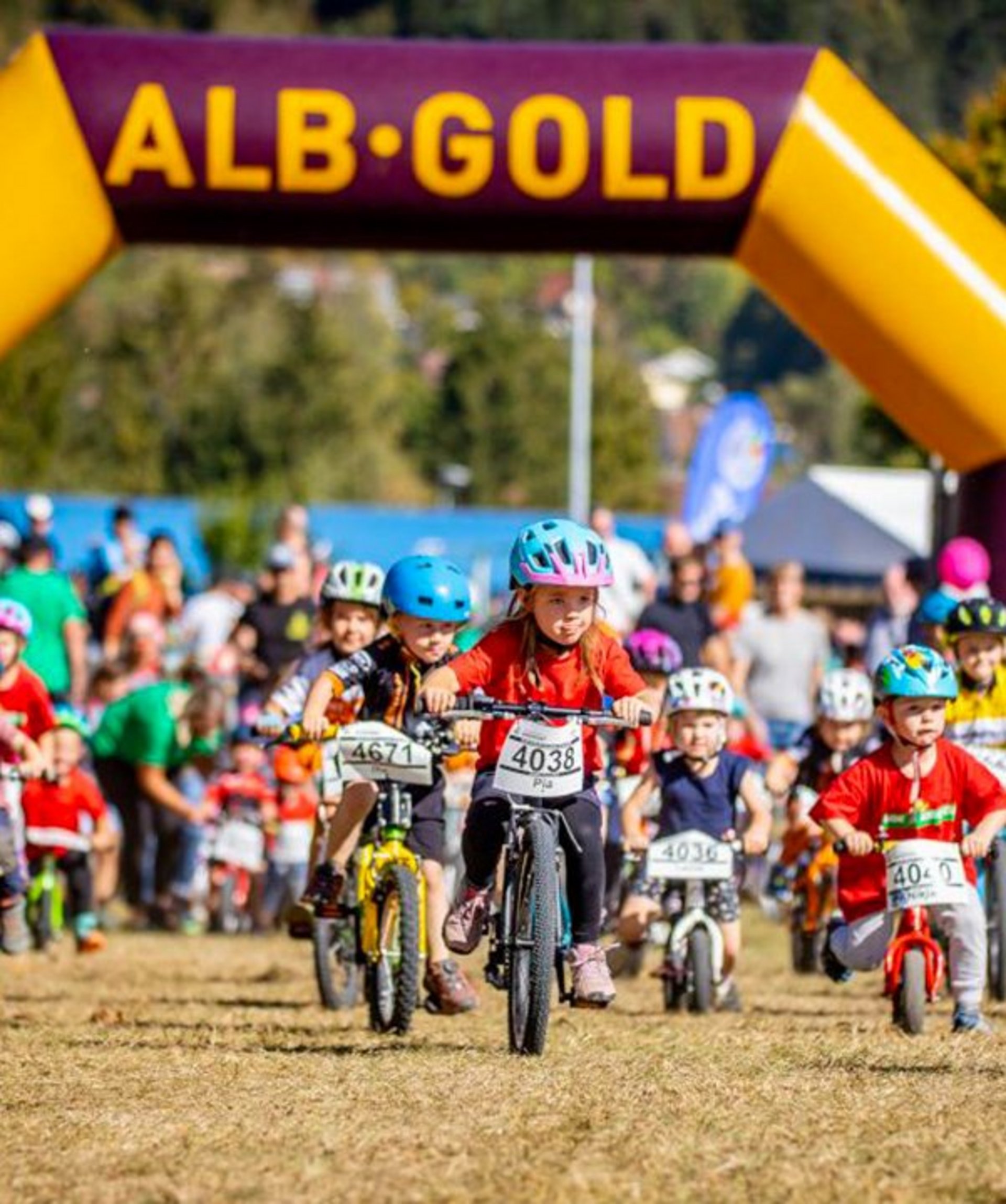Kinder starten ein Fahrradrennen unter einem gelb-lila Tor mit der Aufschrift 'ALB-GOLD'