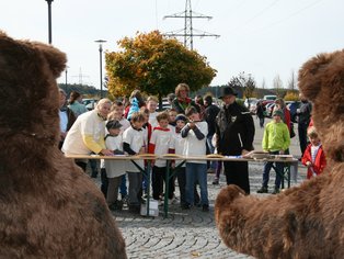 Menschen beobachten eine Veranstaltung im Freien, im Vordergrund zwei große Bärenkostüme