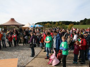 Große Menschenmenge bei einer Veranstaltung im Freien auf gepflastertem Platz mit Zelten im Hintergrund