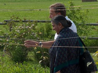 Zwei Personen, die in einer grünen Landschaft spazieren gehen, darunter auch Vandana Shiva.