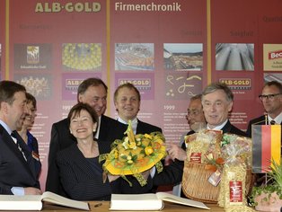 Eine lächelnde Menschengruppe, die Geschenke in der Hand halten unter anderem auch ein selbstgemachter Nudel Blumenstrauß.
