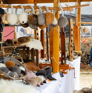 Marktstand mit verschiedenen Fellmützen und Fellwaren auf einem weißen Tuch unter einem Holzgestell mit Lichterkette