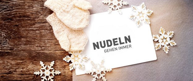 Ein Bild von einer weißen Karte mit dem Text 'NUDELN GEHEN IMMER', umgeben von Schneeflocken und warmen Handschuhen.