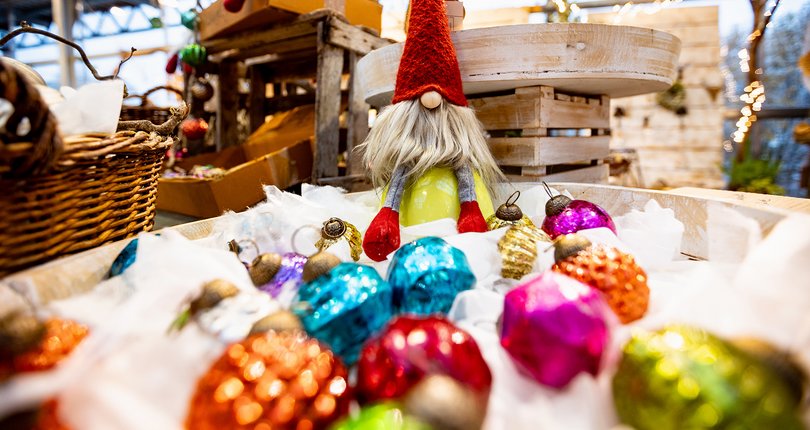 Ein Weihnachtsgnom steht zwischen bunten Weihnachtskugeln.