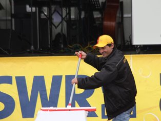 Ein Mann mit einem Besen in der Hand steht vor einer Bühne mit einer Beschriftung "SWR 3".