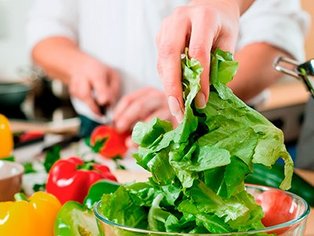 Eine Küchenhilfe, die gerade frisches Gemüse wie Tomaten, Paprika und Salat schneidet.