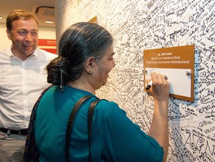 Dr. Vandana Shiva verewigt sich mit einer Unterschrift auf einem Schild an einer großen Wand.