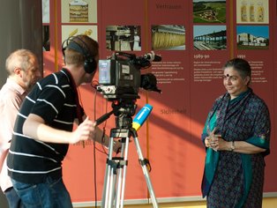 Ein Fernsehteam filmt eine Frau in einem Ausstellungsraum.