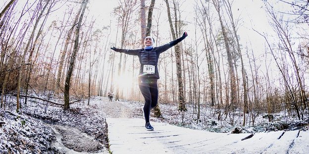 Ein Läufer, der die arme in einer Winterlandschaft in einem Wald ausbreitet.