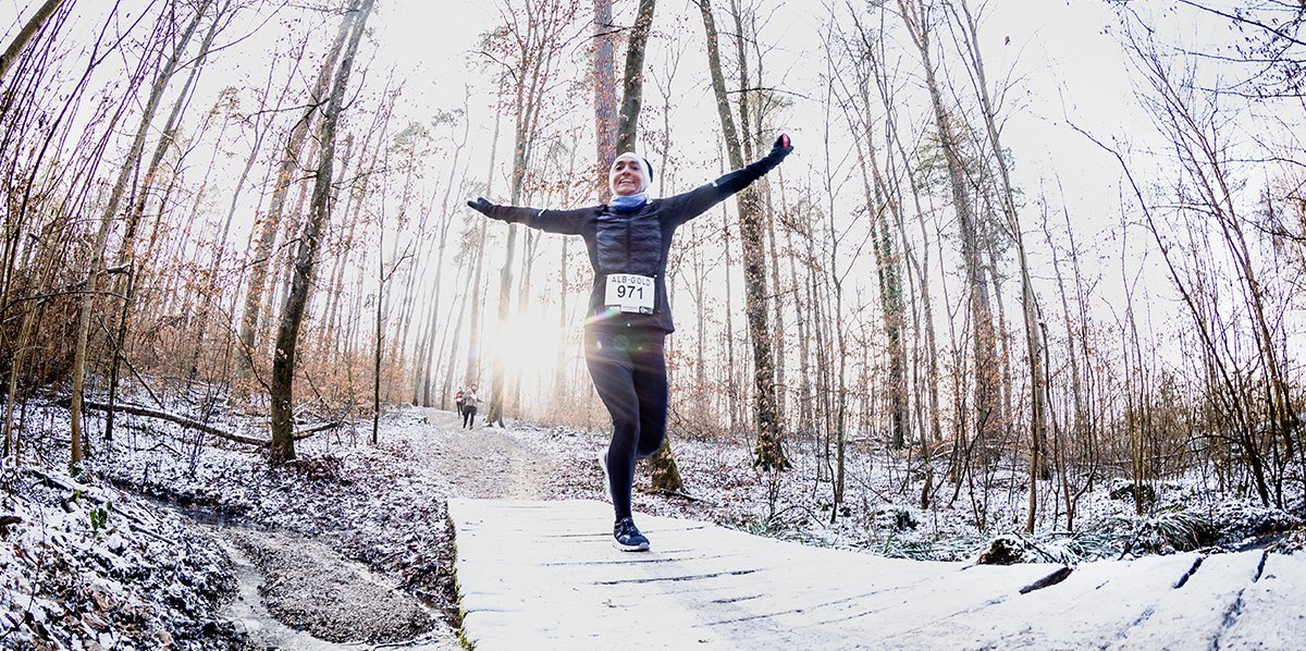 Ein Läufer, der die arme in einer Winterlandschaft in einem Wald ausbreitet.