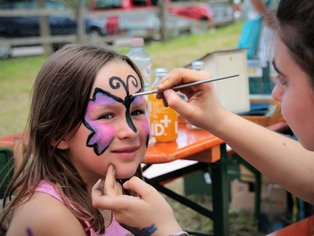 Ein Mädchen bekommt einen Schmetterling auf das Gesicht gemalt.