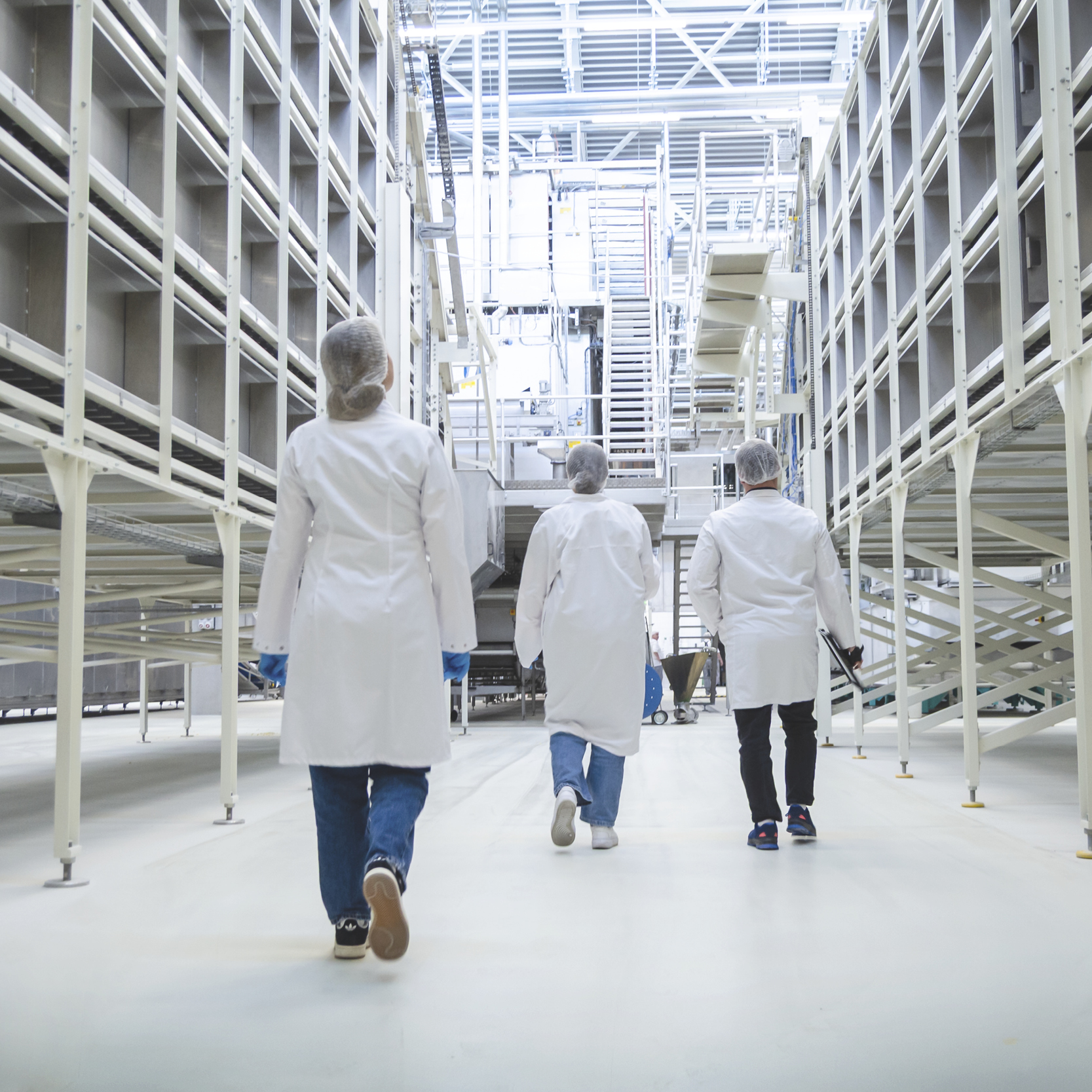 Drei Menschen in Schutzkleidung, die durch die Lagerhallen laufen.